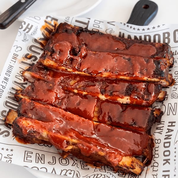 Close-up of a rack of BBQ ribs covered in rich, red sauce, served on branded paper.